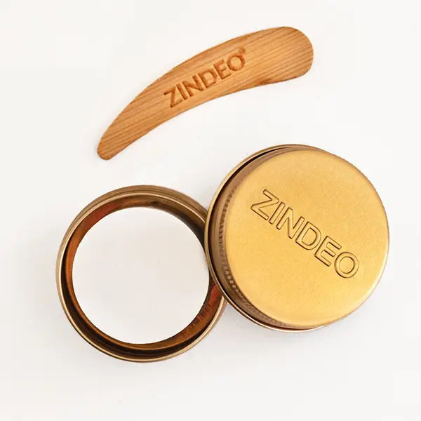 Open gold ZINDEO deodorant tin with its lid and a wooden ZINDEO spatula on a white background