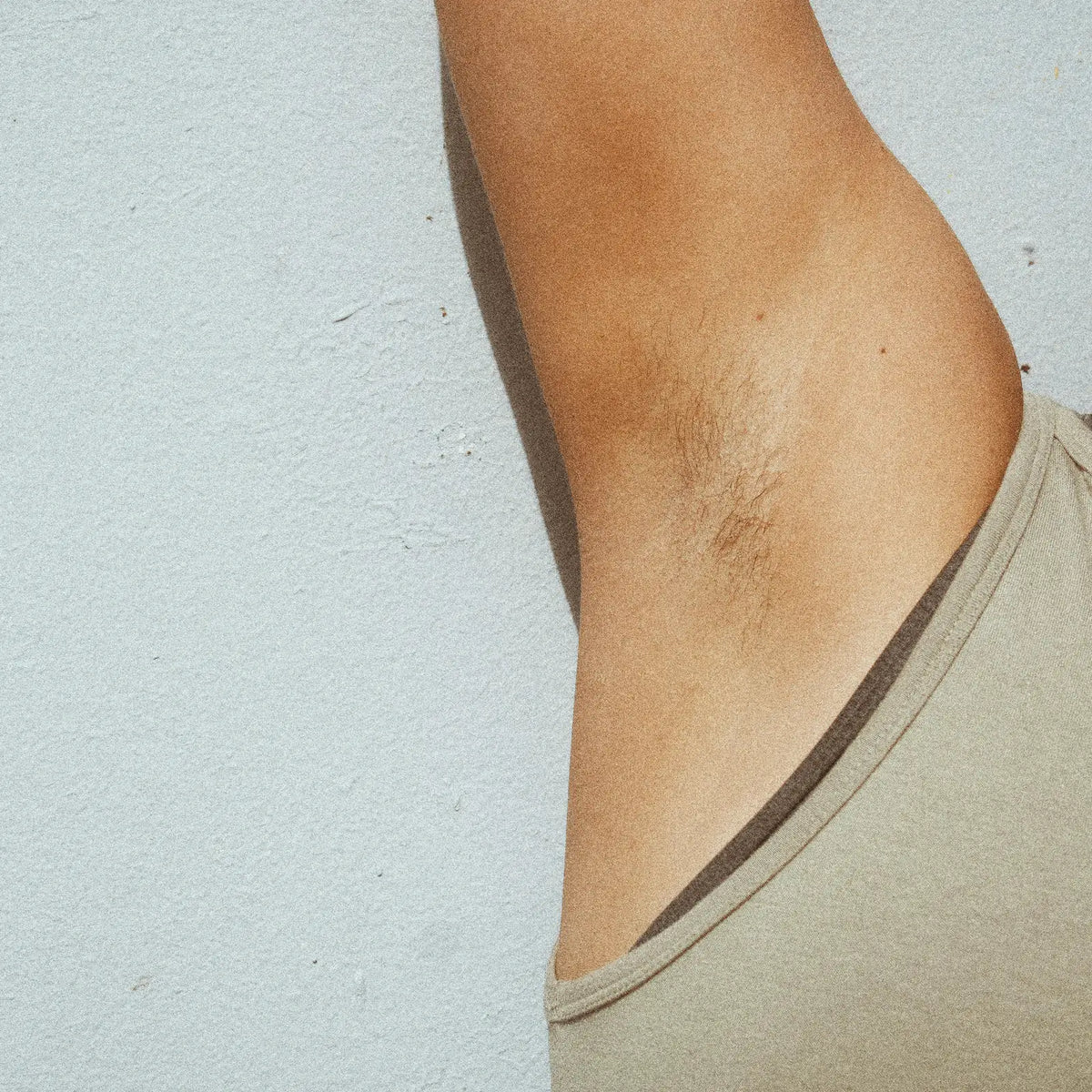 Close-up of a person's raised underarm wearing a beige tank top against a light background