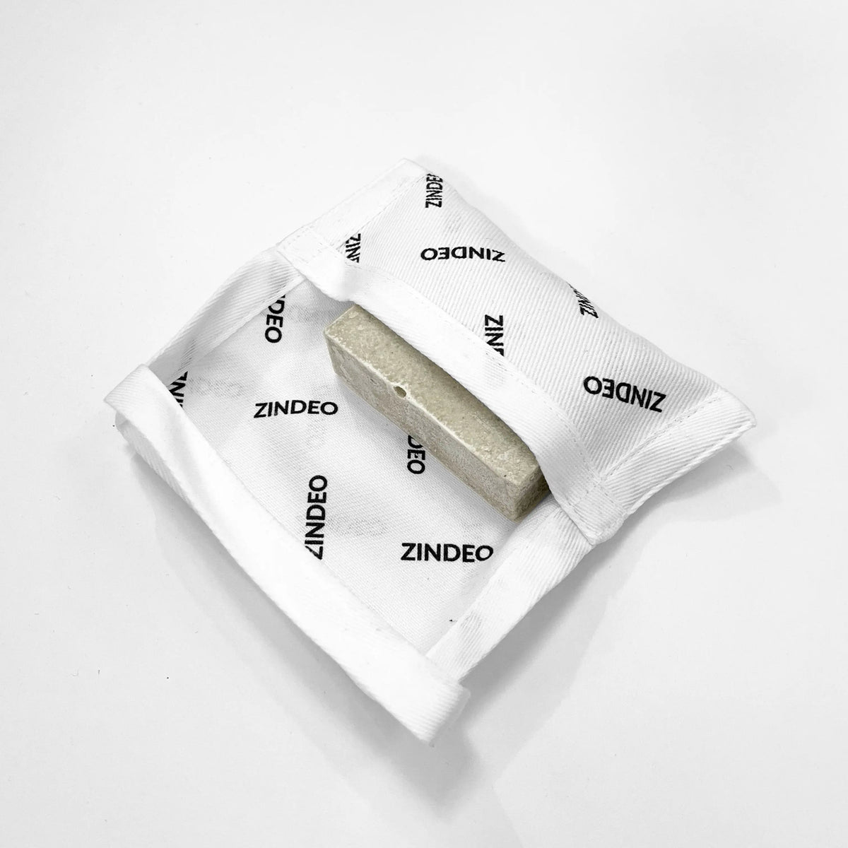 A natural soap bar resting on an open white ZINDEO-branded cotton pouch