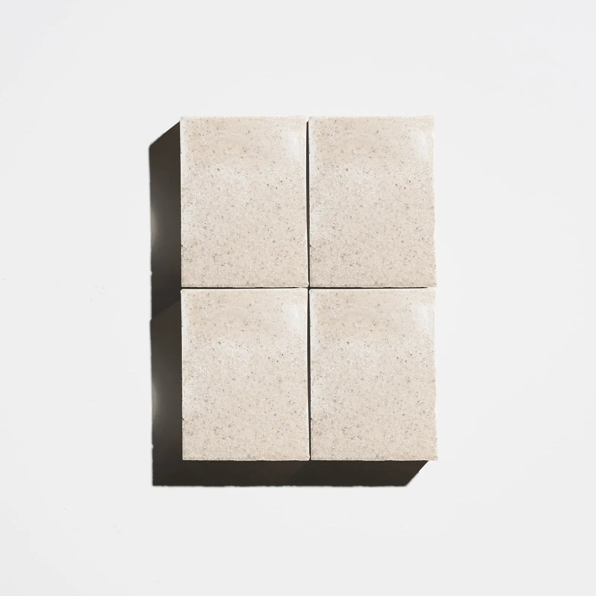 Four square natural beige soap bars arranged in a 2x2 grid on a light background