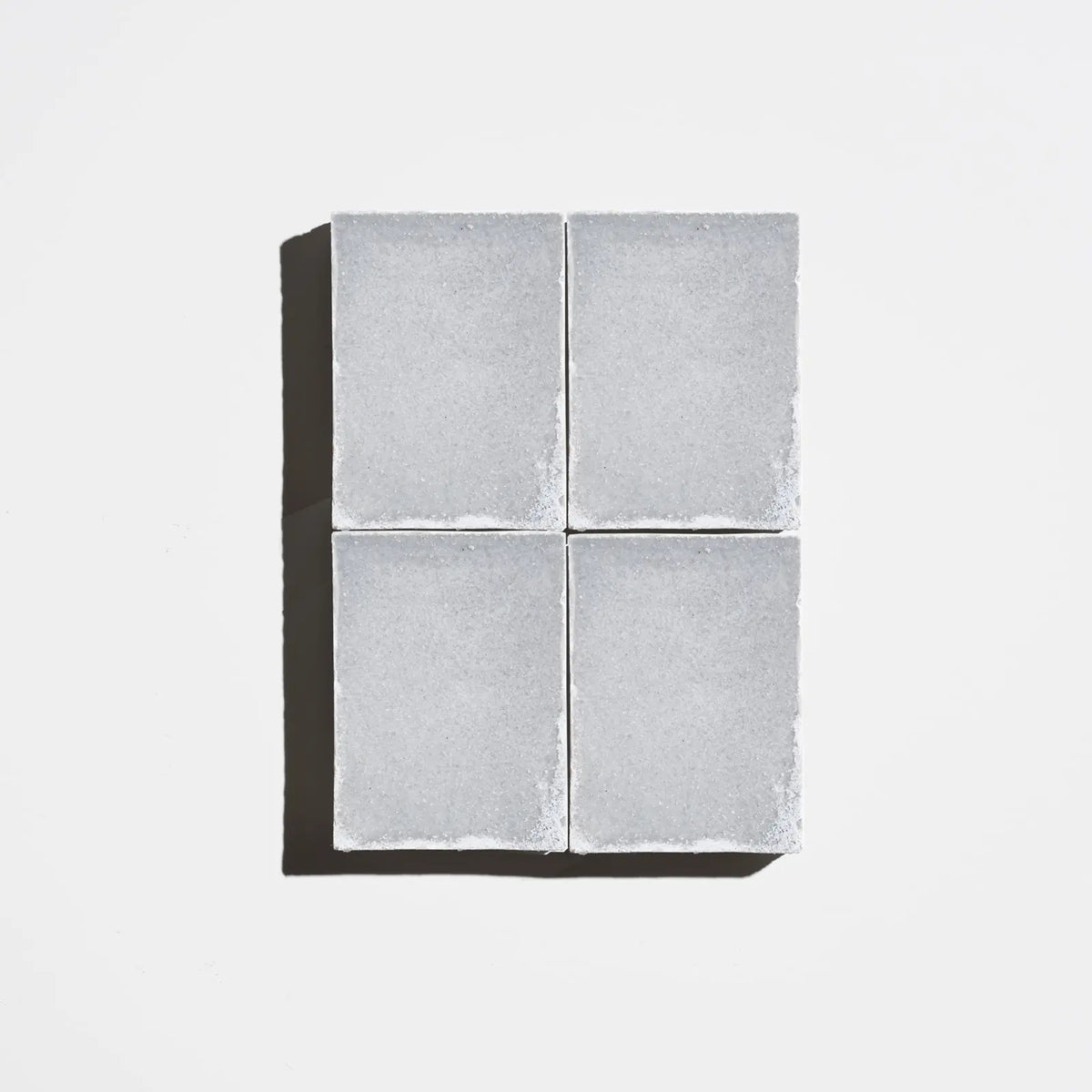 Four square charcoal-gray natural soap bars arranged in a 2x2 grid on a light background