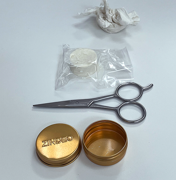 Empty gold ZINDEO tin with a packaged deodorant refill and scissors on a white surface