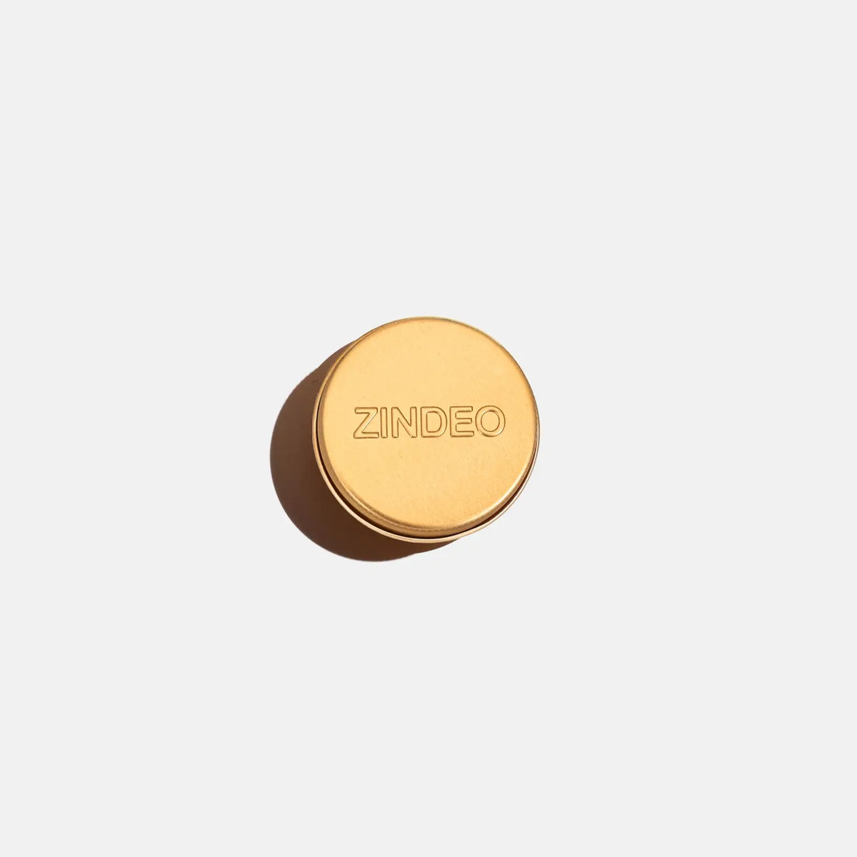 A closed round gold ZINDEO deodorant tin on a light background