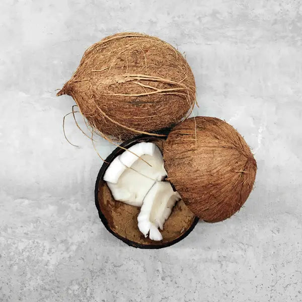 Whole coconuts and a cracked-open coconut showing white flesh on a light gray surface