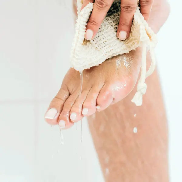 A person washing their foot with a woven soap pouch under running water