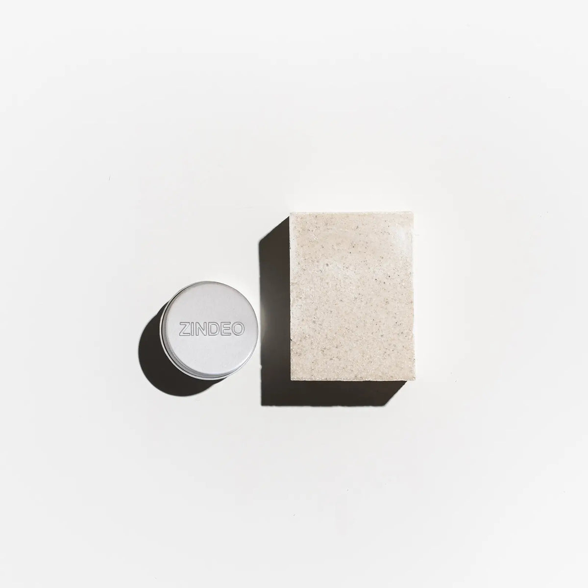 Flat-lay of a silver ZINDEO deodorant tin beside a natural soap bar on a light background