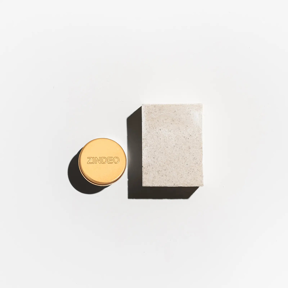 Flat-lay of a gold ZINDEO deodorant tin beside a natural soap bar on a light background