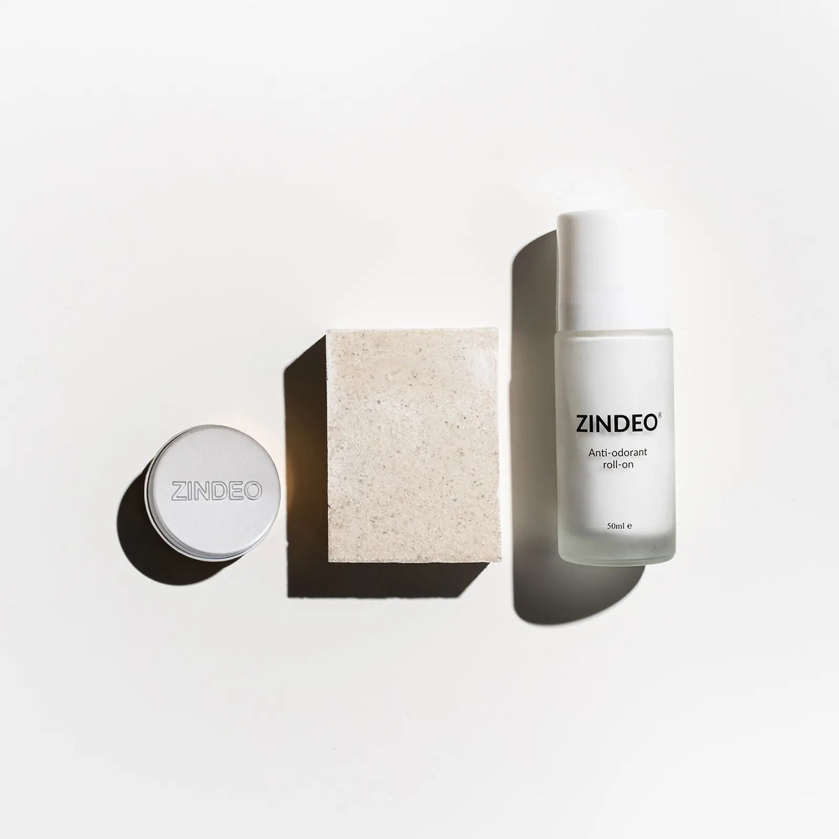 Flat-lay of a silver ZINDEO tin, a natural soap bar and a white ZINDEO anti-odorant roll-on