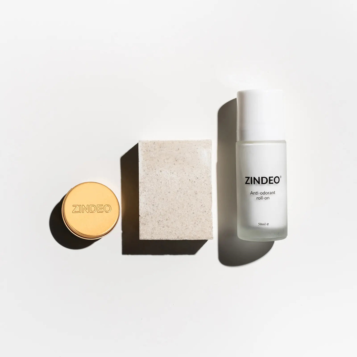 Flat-lay of a gold ZINDEO tin, a natural soap bar and a white ZINDEO anti-odorant roll-on